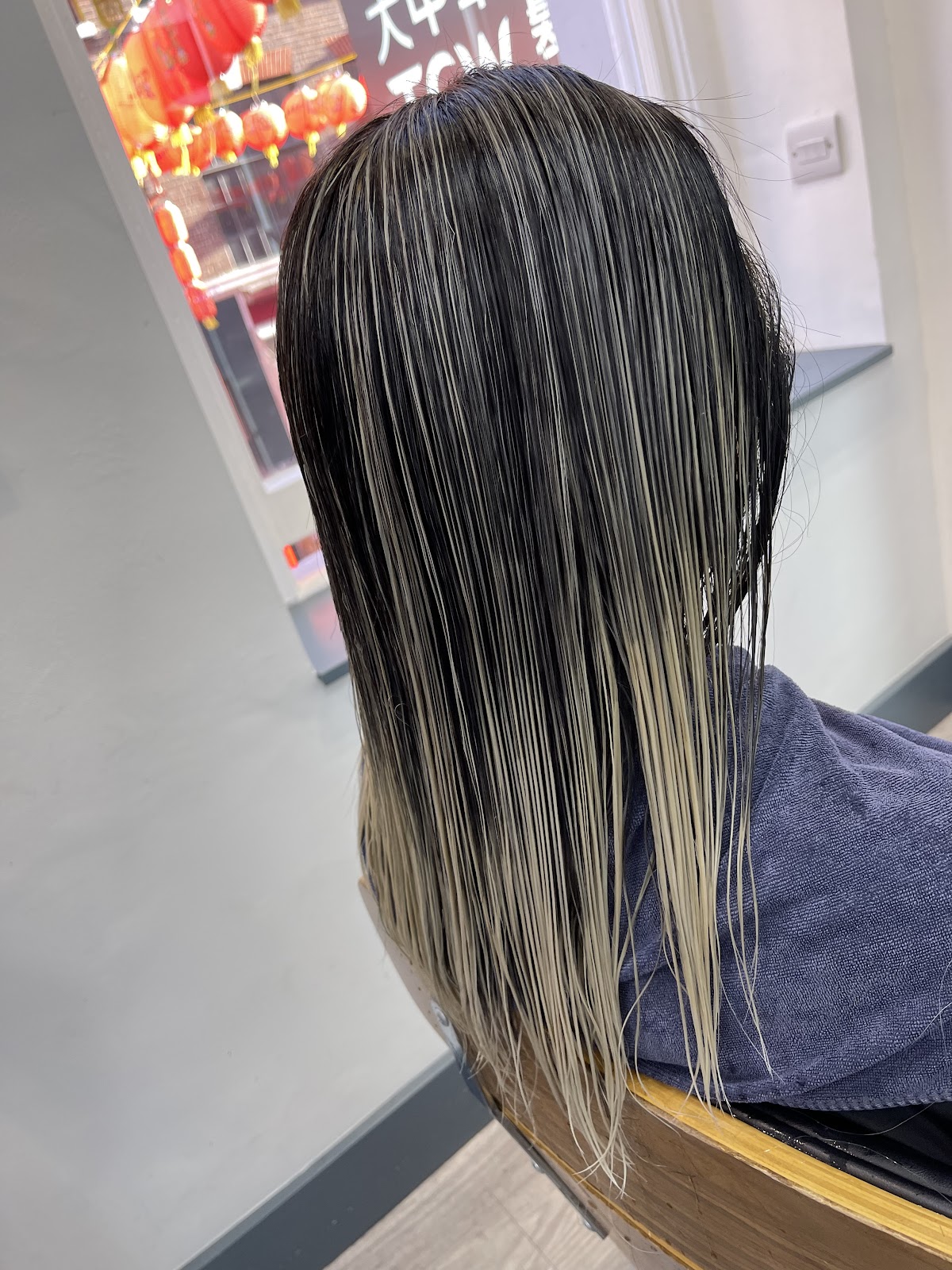 Finished platinum highlights streaked through long dark hair, with red lanterns visible through the salon window behind.