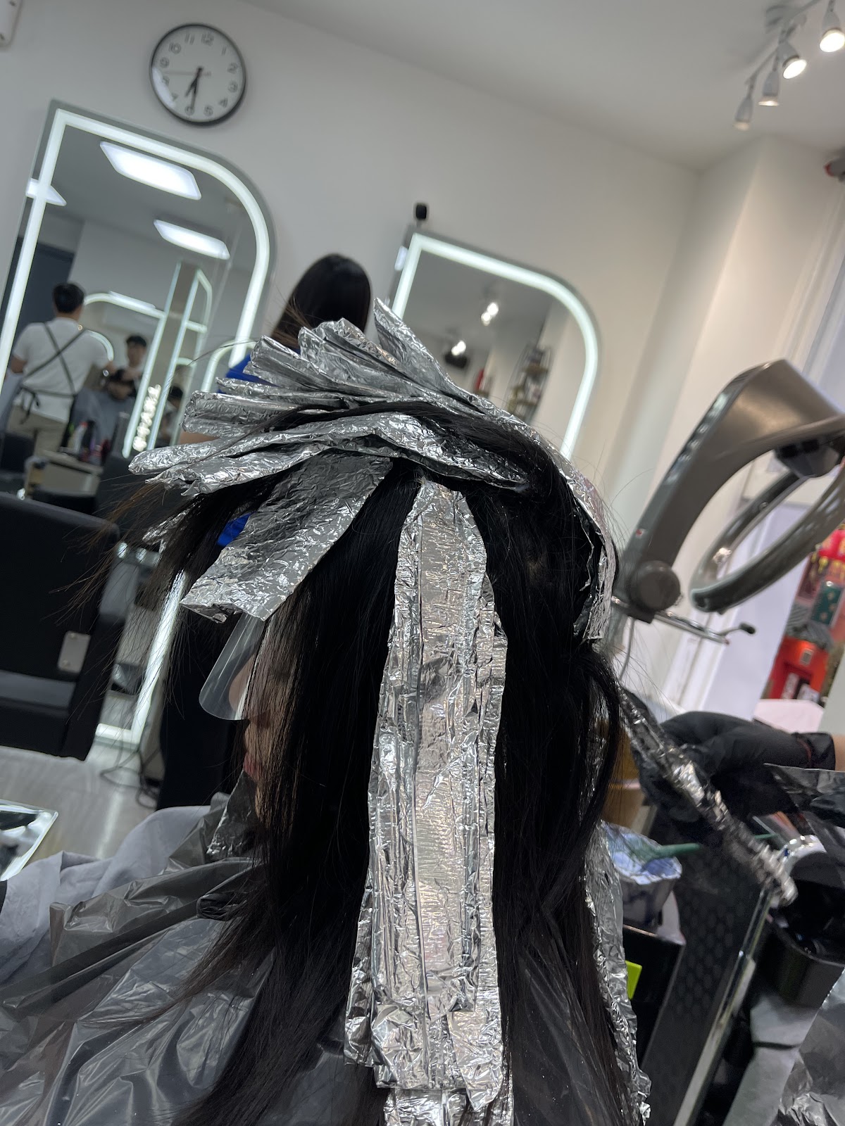 Foils fanned out through long black hair, with the salon's arched mirrors and wall clock in the background.